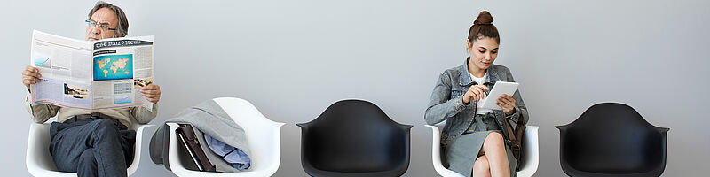 AdobeStock_166067146 zwei Menschen die in einem Warteraum auf Stühlen sitzen