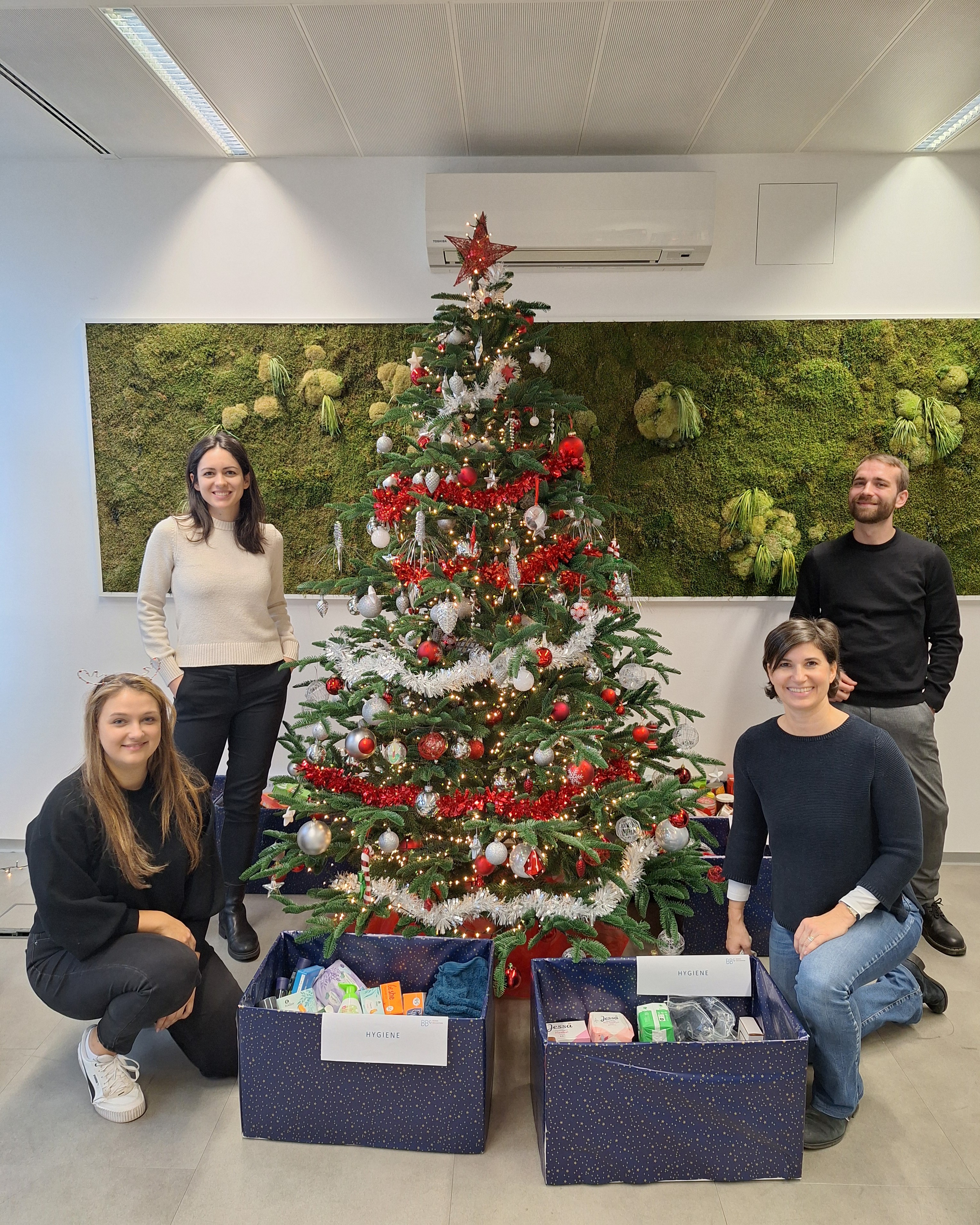 Mitarbeiter und Mitarbeiterinnen der BBG vor einem geschmückten Christbaum mit den Spendenboxen im Vordergrund