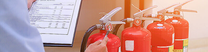 Feuerlöscher Drei Feuerlöscher werden von einem Menschen mit Klemmbrett in der Hand geprüft