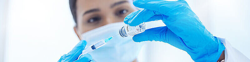 AdobeStock_671459410 Medizinisches Personal zieht Impfstoff in Injektionsnadel auf