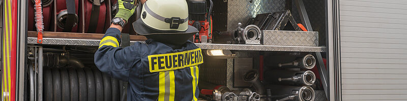 Feuerwehrausrüstung_AdobeStock_281507192 Ein Feuerwehrmann räumt Material ins Feuerwehrauto ein
